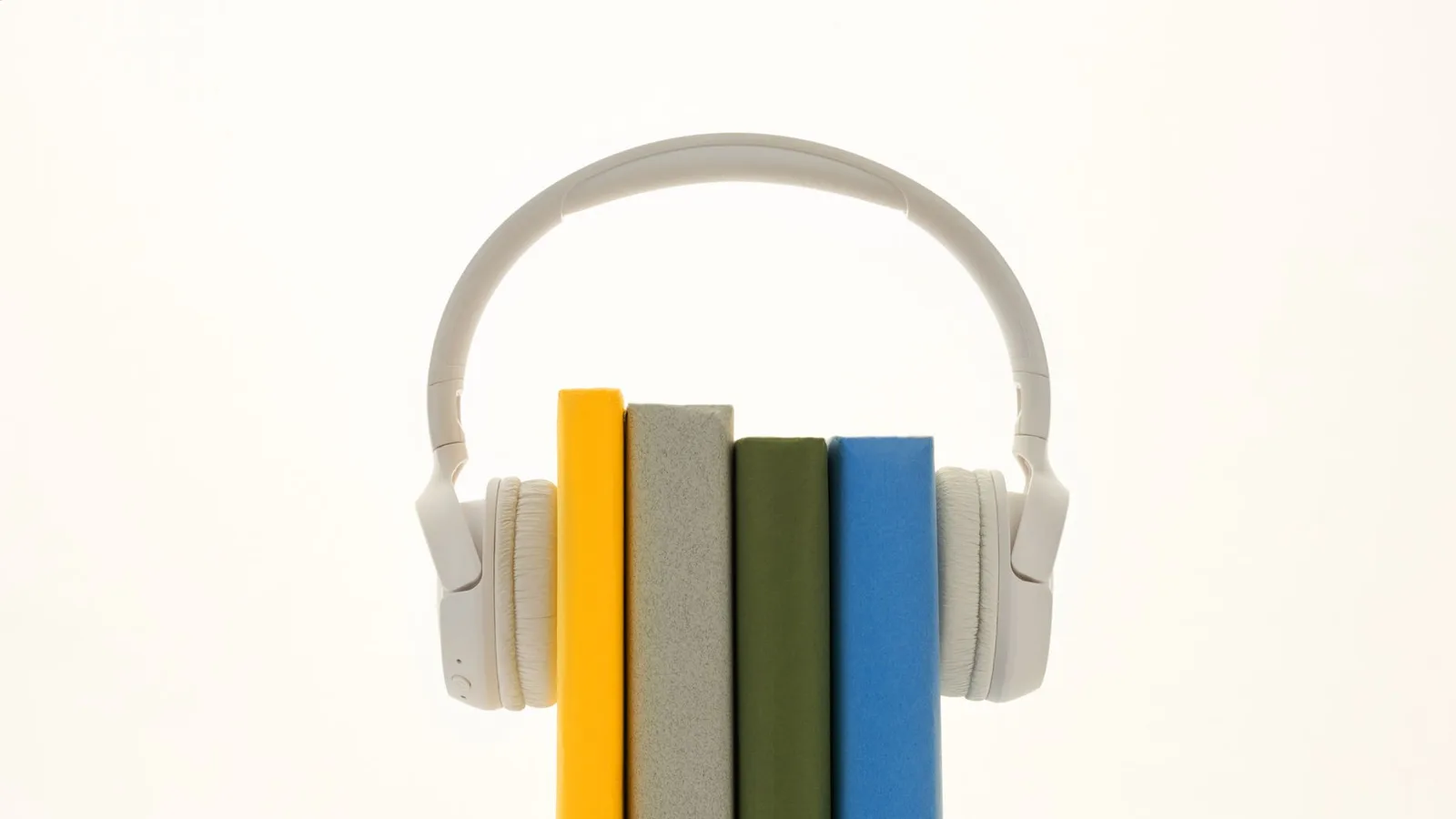 White over-ear headphones resting on a stack of colorful hardback books