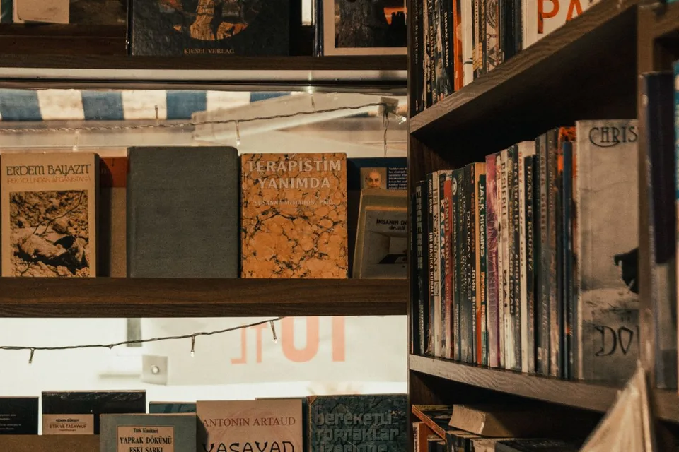 A cozy bookshop with warmly lit wooden shelves full of books, the kind of place where a reader turns a book over to read the back cover
