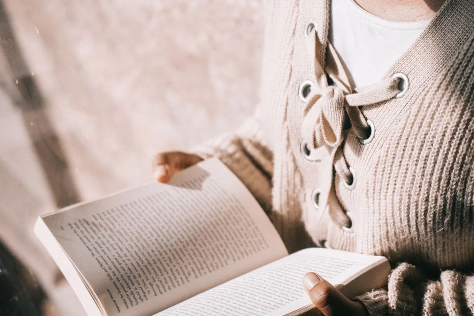 A reader holding an open paperback advance reader copy by a sunlit window