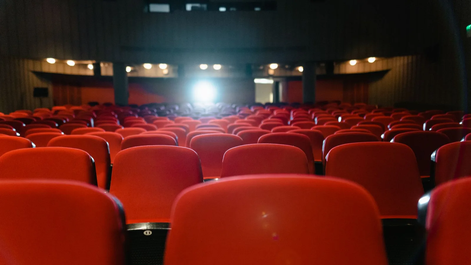 Rows of empty red seats facing an illuminated cinema screen