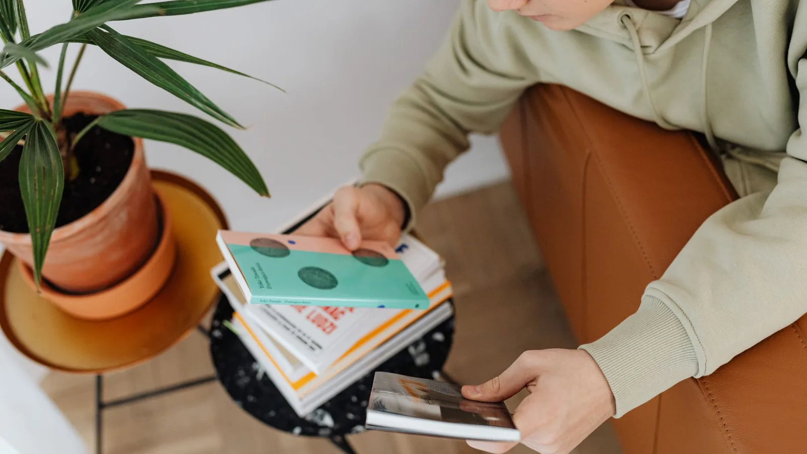 A reader choosing a single book from a stack at home