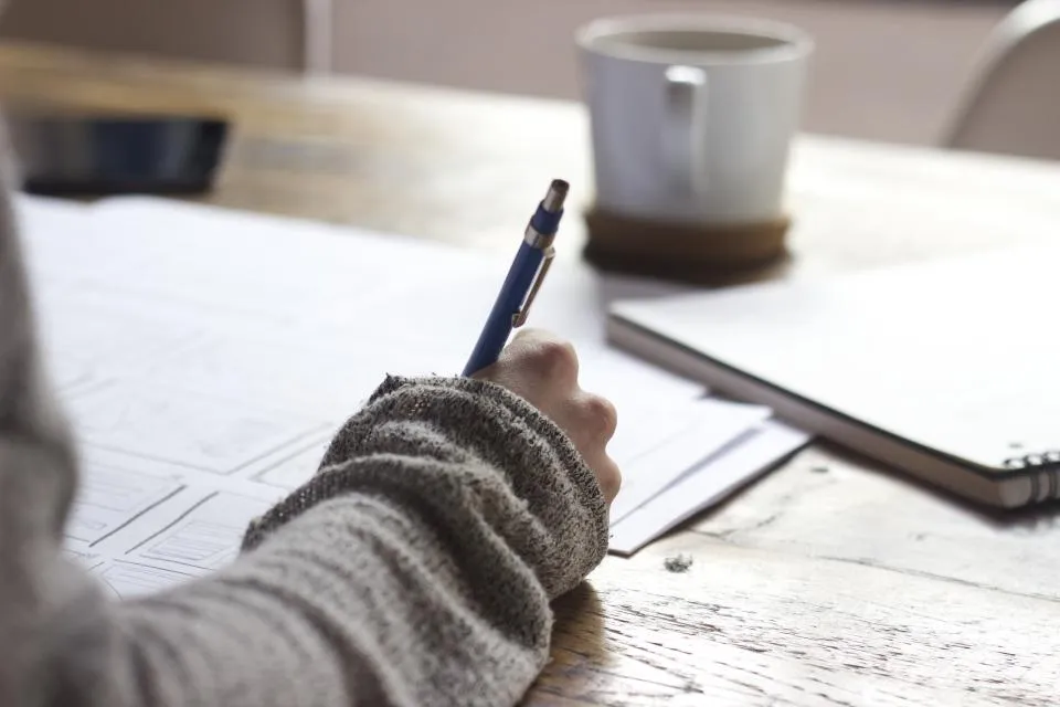 A writer drafting longhand in a notebook beside a cup of coffee